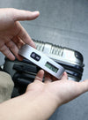 Hand holding Travel Inspira portable digital hanging luggage scale showing clear backlit LCD reading