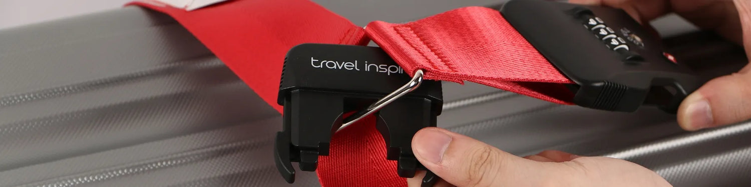 A close-up of a red Travel Inspira luggage strap being fastened with a black buckle. The strap is being secured around a grey suitcase, highlighting the brand's travel accessories. Keywords: Travel Inspira, Luggage Strap, Travel Accessories